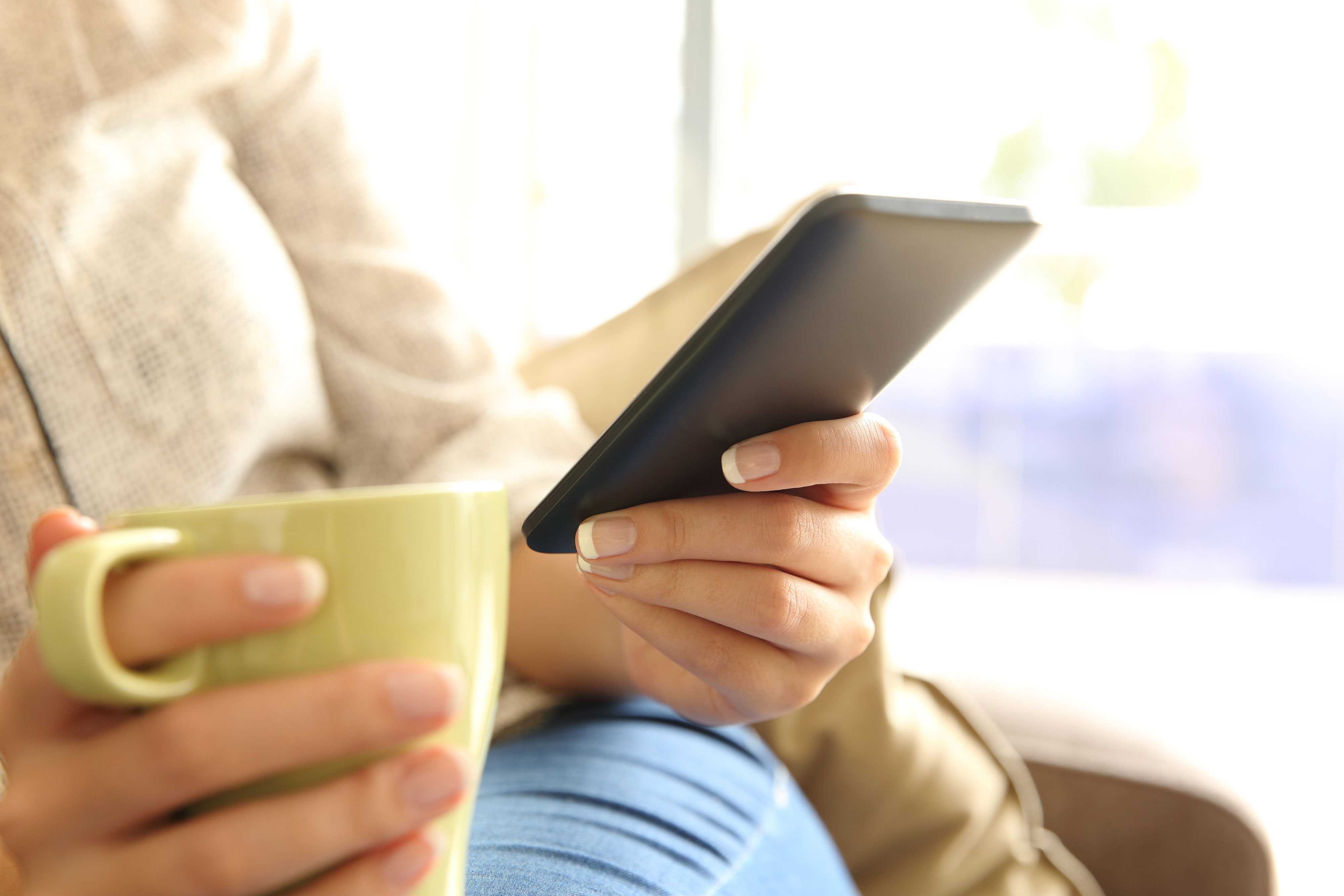 tight image of female sitting in chair with a cup of coffee, looking at their phone